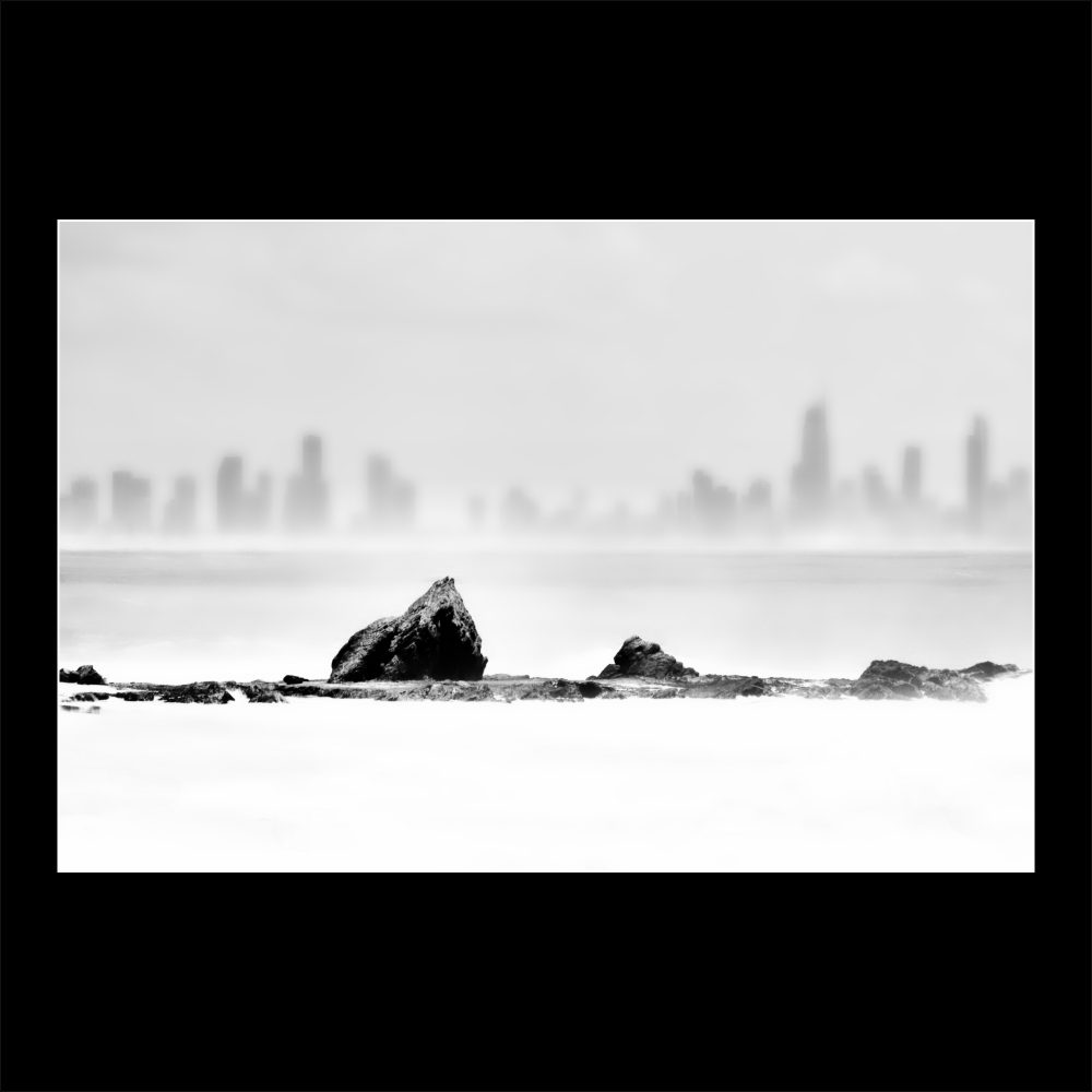 Black and white image of Currumbin Rock with Surfers Paradise skyline in background – Simon Wilson Photography